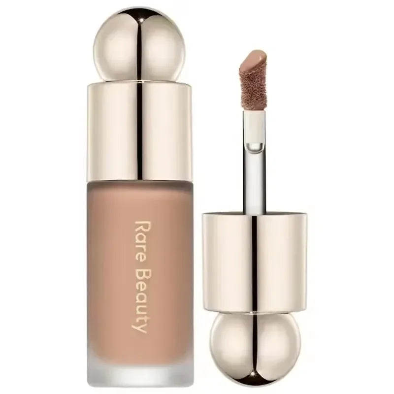 Corrector líquido nude con aplicador y tapa dorada, maquillaje Rare Beauty.