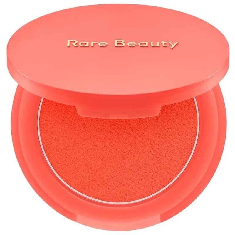 Rubor en polvo compacto coral con estuche redondo, maquillaje Rare Beauty.