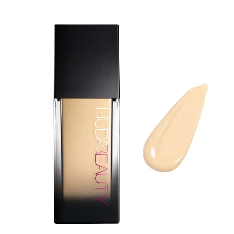 Base de maquillaje líquido tono claro con envase negro y muestra de color beige.